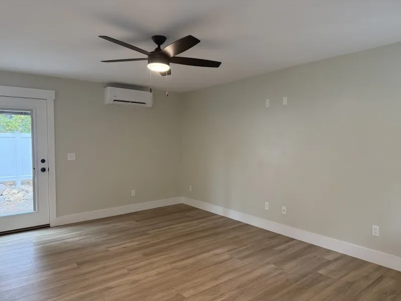 Empty room with wood floors, ceiling fan, light gray walls, and a glass door to the left.
