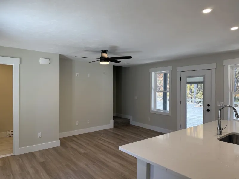 Open-concept room with light wood floors, white walls, a ceiling fan, and large windows.