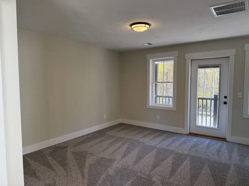 Empty room with gray carpet, light walls, two windows, and a glass door to a balcony.