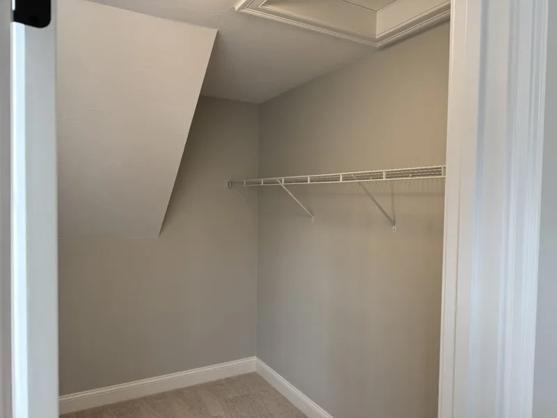 Empty walk-in closet with beige walls, sloped ceiling, and a wire shelf on the right wall.