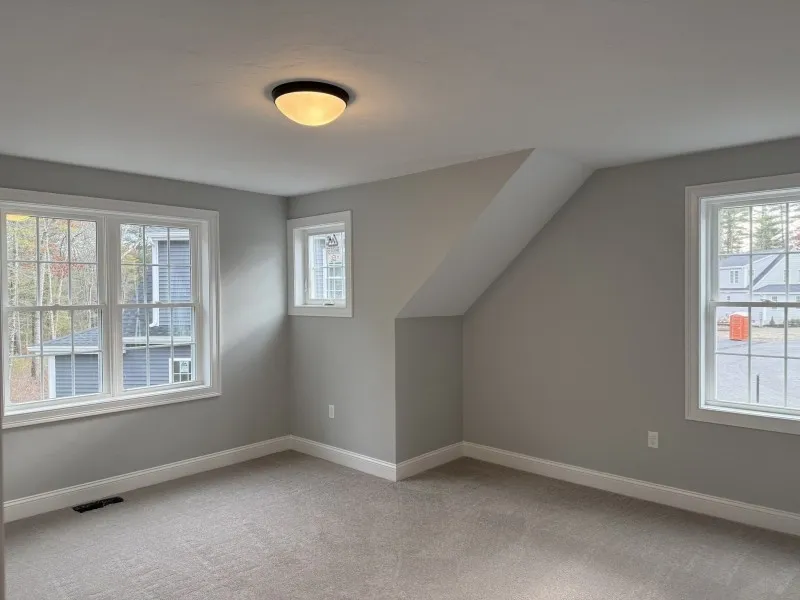 Empty gray-carpeted room with three windows, gray walls, and a ceiling light fixture.