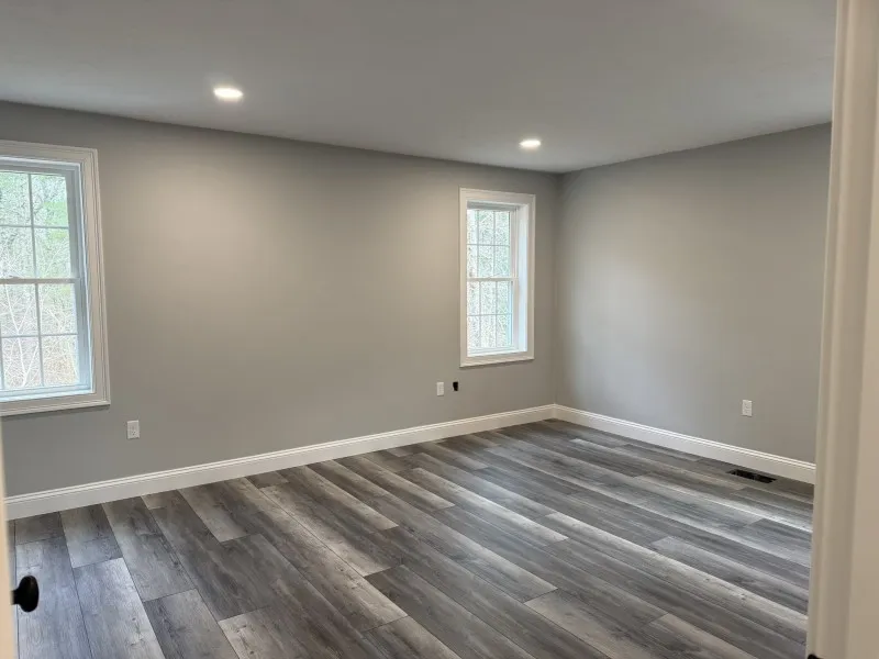 Empty room with gray walls, wood flooring, and two windows letting in natural light.