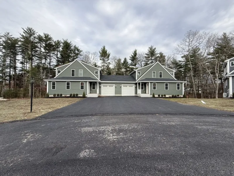 Duplex house with two garages, green siding, and a wide driveway on a cloudy day.