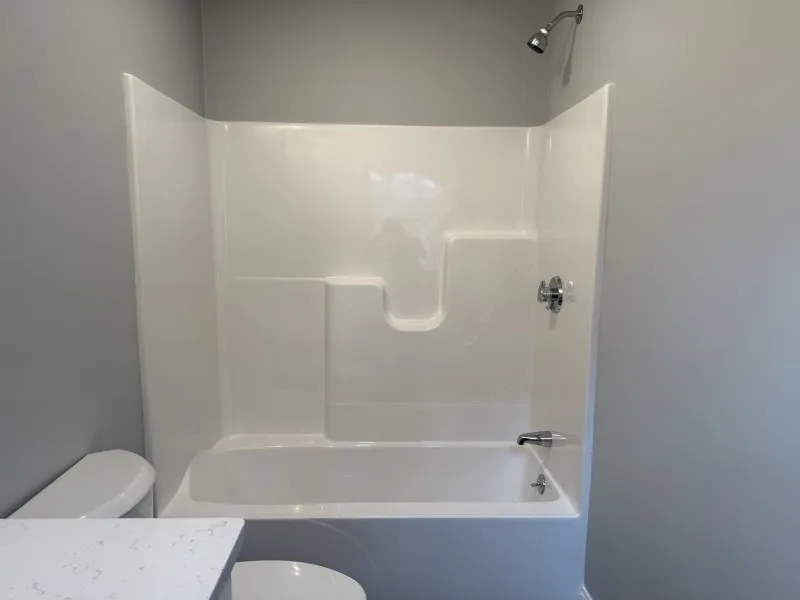 White bathtub with built-in shower, white walls, and a toilet partially visible on the left.